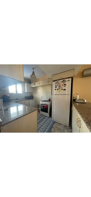 A kitchen with granite countertops, a refrigerator with magnets, a stove, and a chandelier.