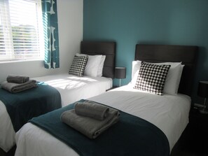 A hotel room with two beds, each with a headboard, white bedding, and a teal accent wall. - Pet Friendly Cottage with Sea Views (Saundersfoot)
