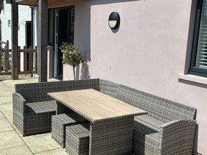 A wicker outdoor seating area with a table, a potted plant, and a wall-mounted light fixture. - Pet Friendly Cottage with Sea Views (Saundersfoot)