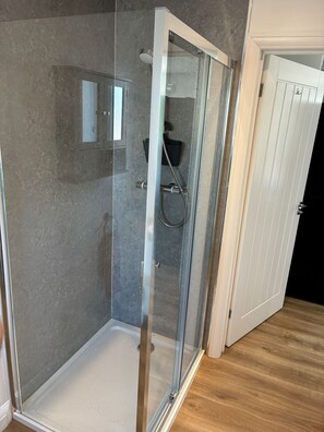 A glass-enclosed shower with a white door, a towel rack, and a wooden floor. - Pet Friendly Cottage with Sea Views (Saundersfoot)