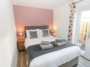 A neatly made bed with pillows, a bedside table with a lamp, and a view through a glass door. - Pet Friendly Cottage with Sea Views (Saundersfoot)