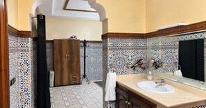 Ένα μπάνιο με μια ξύλινη ντουλάπα, έναν νιπτήρα με καθρέφτη και διακοσμητικά πλακάκια.