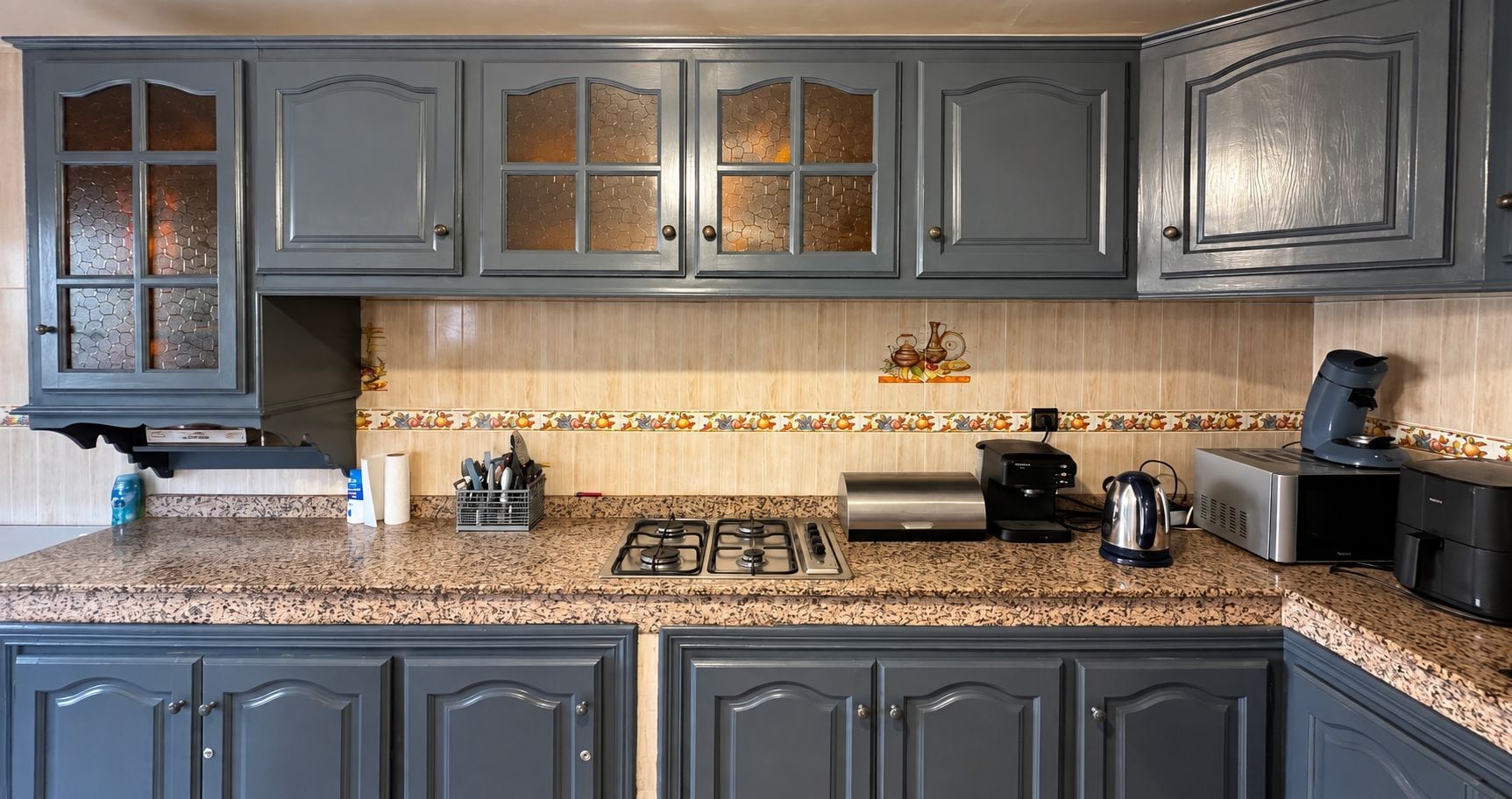 A kitchen with dark cabinets, a granite countertop, a stove, a coffee maker, and a toaster.