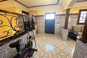 Una habitación con una bicicleta estática, paredes con diseño y una ventana.