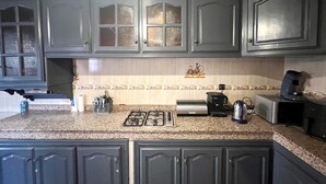 Une cuisine dotée de plans de travail en granit, de meubles de rangement sombres, d’une cuisinière à gaz, d’une machine à café et d’un grille-pain.
