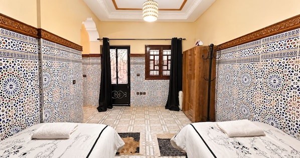 A room with two beds, a wooden door, patterned walls, and a chandelier.