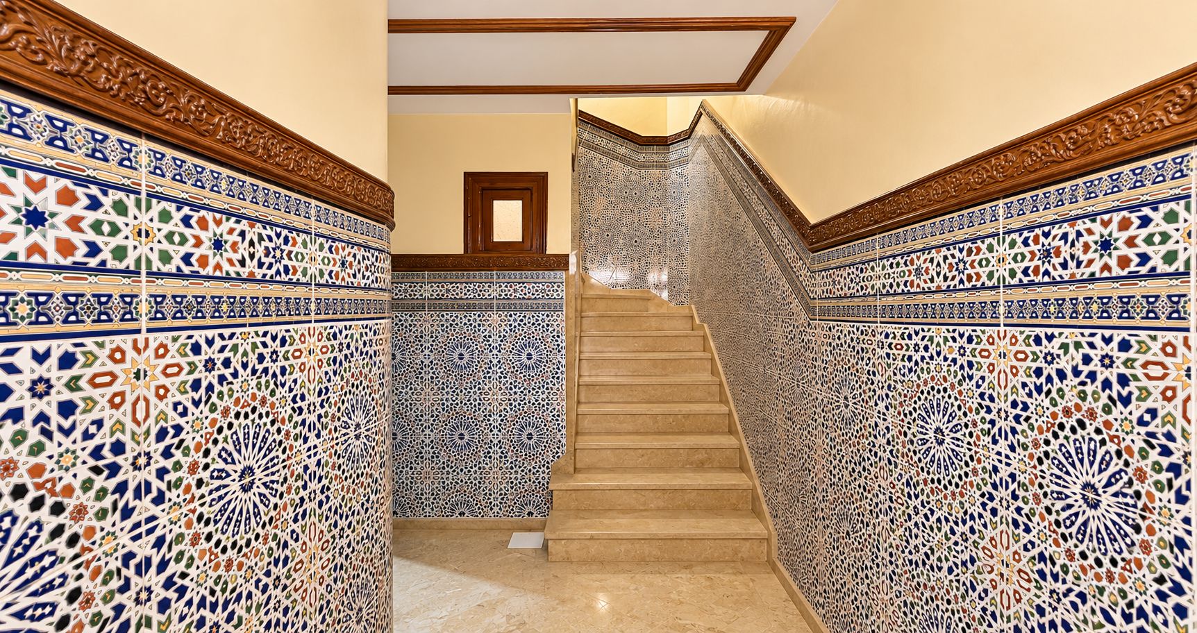 Un escalier orné de motifs complexes en carreaux sur les murs et doté d’une main courante en bois.