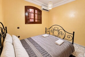 Un dormitorio con cama, almohadas, ventana y lámpara en el techo.