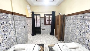 Une pièce dont les murs sont recouverts de carreaux décoratifs, avec une porte en bois et un lit recouvert d’une couverture blanche.