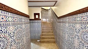 Un escalier orné de motifs complexes en mosaïque de chaque côté, menant à une pièce dont la porte est en bois et se trouve en haut.