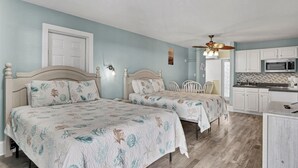 Ein Schlafzimmer mit zwei Betten, einem Deckenventilator und einer Küchenzeile mit weißen Schränken und einer Mikrowelle.