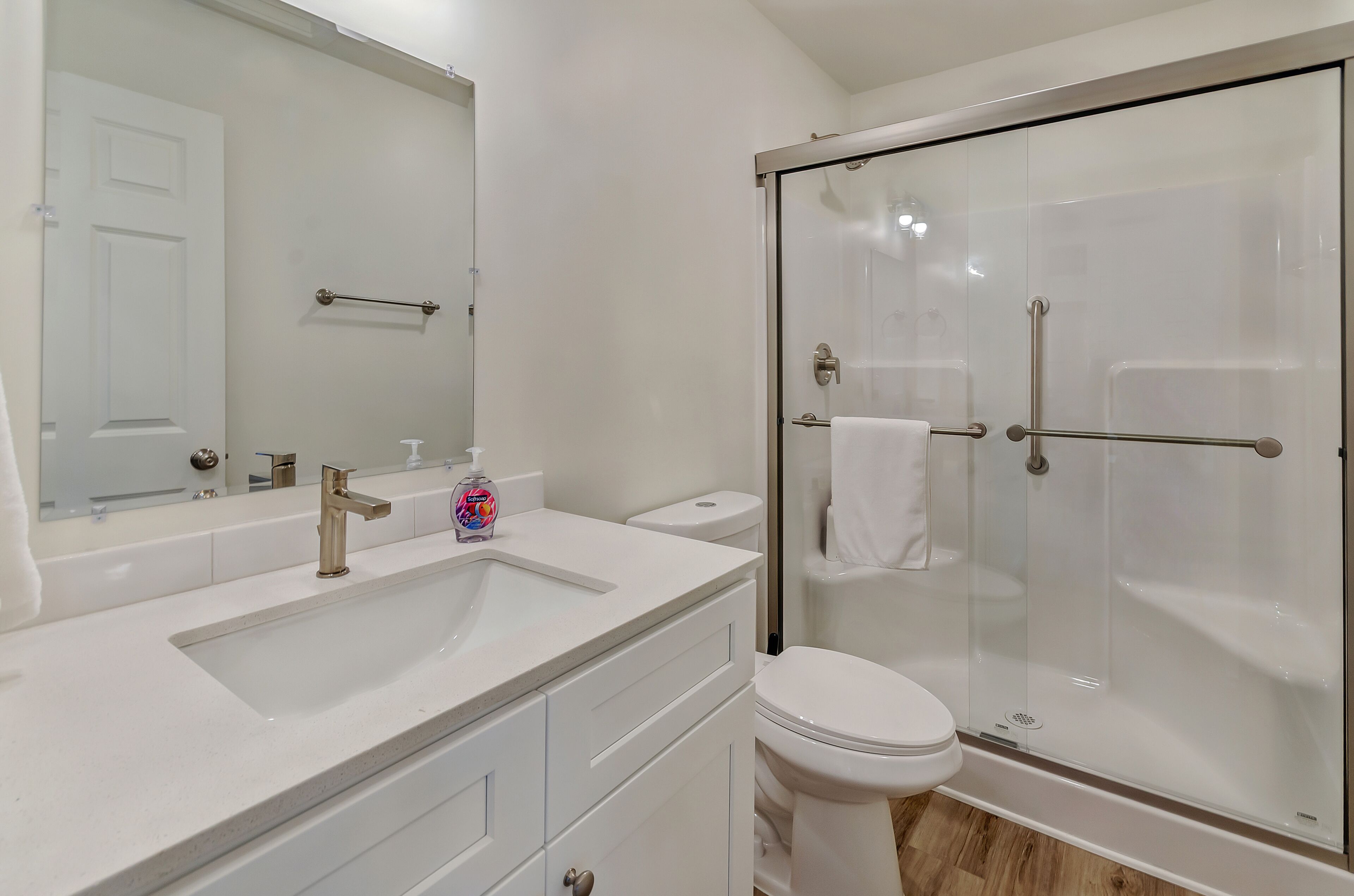 A modern bathroom with a large mirror, a sink, a toilet, and a glass-enclosed shower.