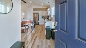 A modern kitchen with white cabinets, a stainless steel refrigerator, and a wooden dining table with chairs. - Scenic New Built Waterfront Cabin on Hammersley Inlet Olympic Peninsula (Shelton)