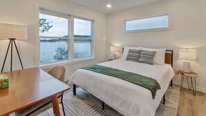 A hotel room with a bed, a desk, a chair, a window with a view of a lake, and two bedside lamps. - Scenic New Built Waterfront Cabin on Hammersley Inlet Olympic Peninsula (Shelton)