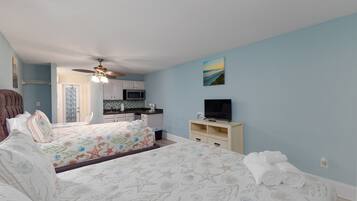 A bedroom with two beds, a TV, and a kitchenette in the background.