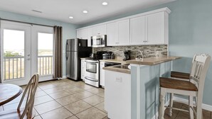 A modern kitchen with white cabinets, stainless steel appliances, and a breakfast bar. - Surf City Getaway– Cozy Suite - Walk to Beach (Surf City)