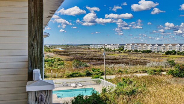 A view from a balcony overlooking a swimming pool, a beach, and a row of white buildings. - Surf City Getaway– Cozy Suite - Walk to Beach (Surf City)