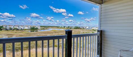 A covered porch with a view of a grassy area and distant buildings.