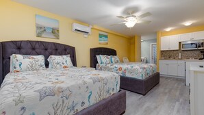 A hotel room with two beds, a ceiling fan, an air conditioner, a kitchen area, and a painting on the wall. - Surf City Getaway - Motel Unit - Walk to Beach (Surf City)