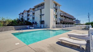 A pool area with lounge chairs, a clear pool, and a multi-story building with balconies. - Surf City Getaway - Motel Unit - Walk to Beach (Surf City)