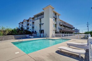 A pool area with lounge chairs, a clear pool, and a multi-story building with balconies. - Surf City Getaway - Motel Unit - Walk to Beach (Surf City)