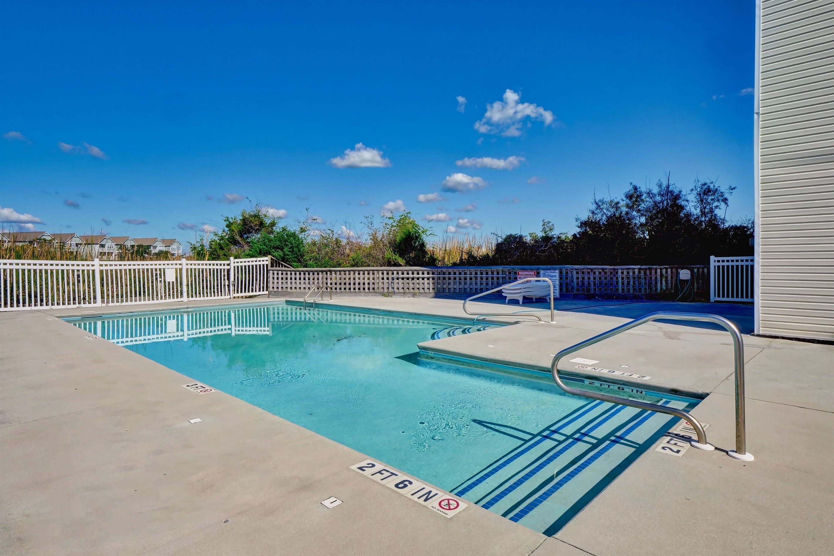 A swimming pool with a white fence, a lifeguard chair, and a clear blue sky.