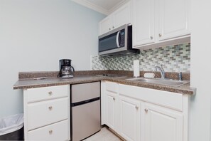 A compact kitchen with white cabinets, a stainless steel dishwasher, a coffee maker, and a microwave. - Surf City– Beachcomber Bungalow motel-Pet Friendly (Surf City)