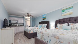 Une chambre avec deux lits, un coin cuisine et un ventilateur de plafond.