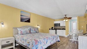 A bedroom with a bed, bedside tables, a nightstand, a ceiling fan, and a view of the kitchen. - Surf City Stay- Motel Unit - Walk to Beach (Surf City)