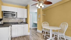A kitchen with white cabinets, a microwave, a coffee maker, and a dining area with a white table and chairs. - Surf City Stay - Motel Unit - Walk to Beach (Surf City)