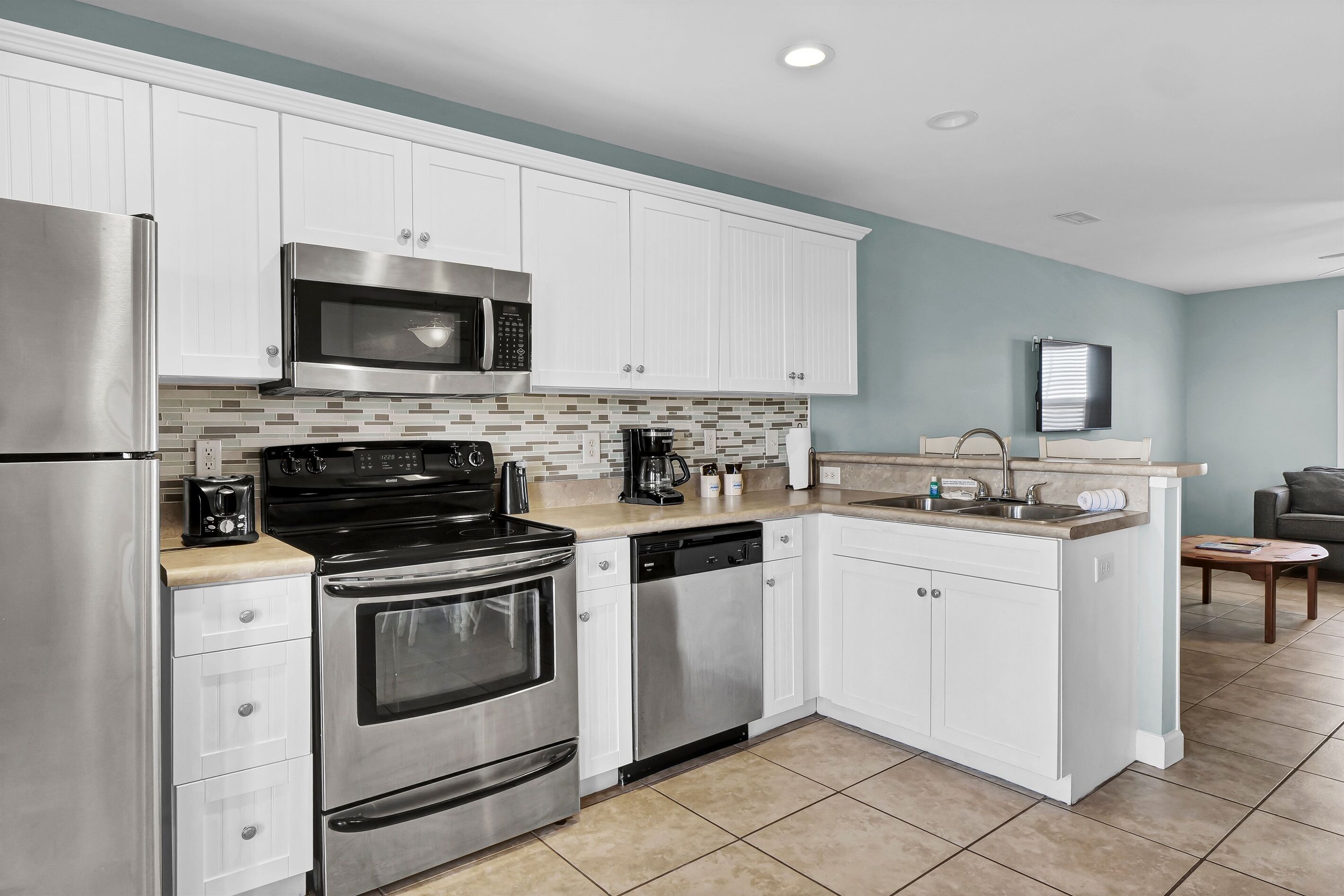 A modern kitchen with white cabinets, stainless steel appliances, and a tiled backsplash.