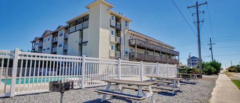 A multi-story building with balconies, a white fence, and picnic tables.