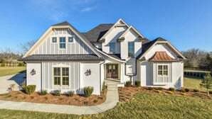 Une maison à deux étages avec une entrée à l’avant, un porche couvert et un jardin aménagé.