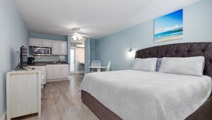 A bedroom with a large bed, a desk, a kitchenette, and a view of the beach. - Surf City Getaway - Walk to Beach - Seasonal Pool (Surf City)