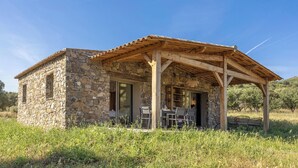 Un edificio de piedra con una pérgola de madera, una mesa y sillas afuera.