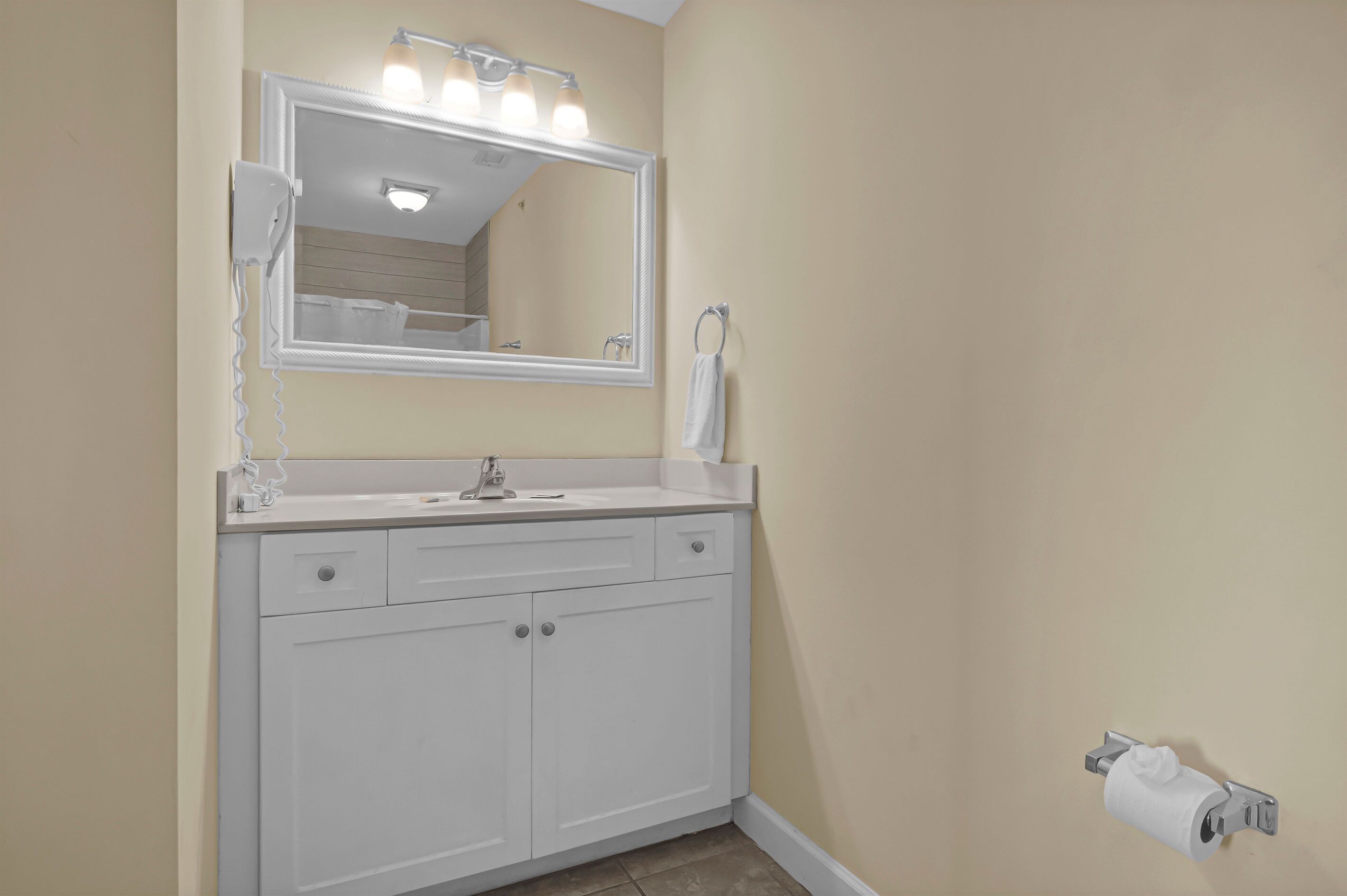 A bathroom with a white vanity, a large mirror with lights, and a towel rack.