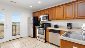 A modern kitchen with wooden cabinets, stainless steel appliances, and a large window overlooking a balcony. - Surf City Getaway- Walk to Beach - Seasonal Pool (Surf City)