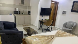A compact hotel room with a bed, a sofa, a small desk with a chair, a TV, and a kitchenette. - HOTL FABY 1 (Dakar)