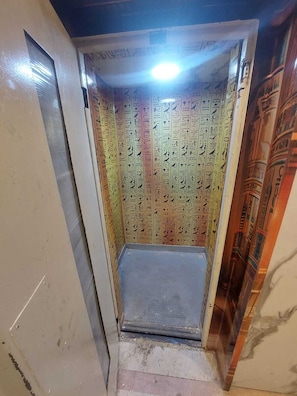 A narrow stairway with a tiled wall featuring hieroglyphs, leading to a landing.
