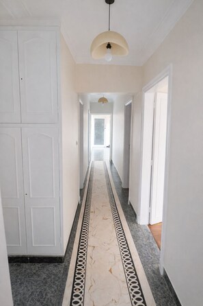 A hallway with white walls, a marble floor with a black and white border, and a pendant light.