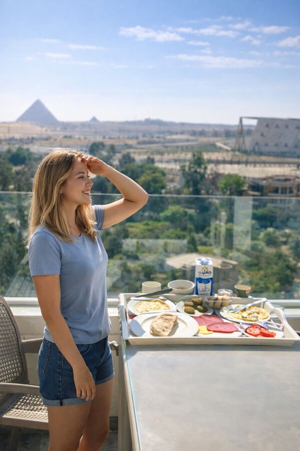 A person standing by a table with a meal on a balcony overlooking a cityscape.