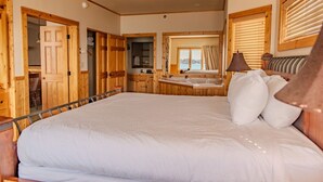 Ruime slaapkamer met een groot bed, houten wanden, een inpandige badkamer en uitzicht op de omgeving.