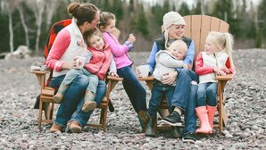 Una familia sentada en sillas de madera al aire libre, con suelo rocoso y árboles de fondo.