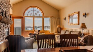 A cozy living room with a stone fireplace, large windows with a view of the water, and wooden furniture. - Lakeview Burlington Bay Two bedroom Suite (Two Harbors)