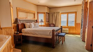 A spacious bedroom with a large bed, a wooden headboard, a bench, and a view of the sea through a window. - Lakeview Burlington Bay Two bedroom Suite (Two Harbors)