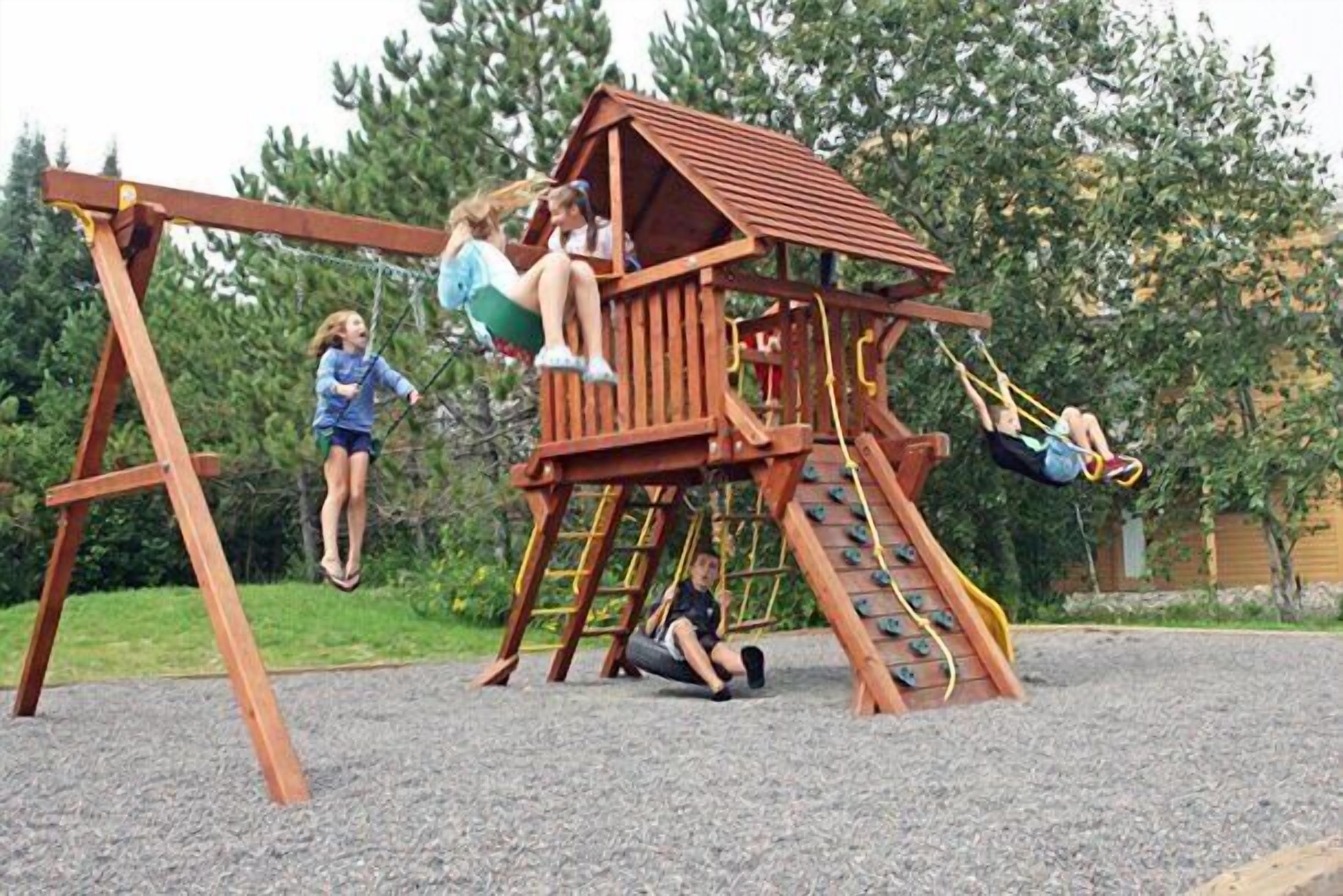 A wooden playground with swings and a climbing structure.