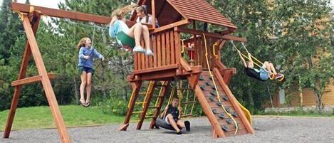 A wooden playground with swings and a climbing structure.