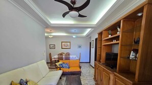 Ein Wohnzimmer mit einer Couch, einem Couchtisch, einem Fernseher auf einem Holzkasten und einem Deckenventilator.
