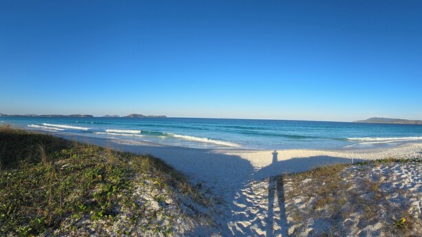 Ein Strand mit blauem Himmel, Wellen und Landformen in der Ferne.