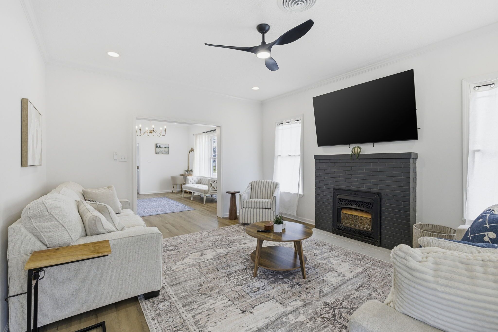 A modern living room with a fireplace, a ceiling fan, and a flat-screen TV mounted on the wall.